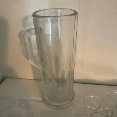 Sale Photo Thumbnail #190: Vintage tall glass beer mug featuring an etched circular logo on the front and a paneled base design.