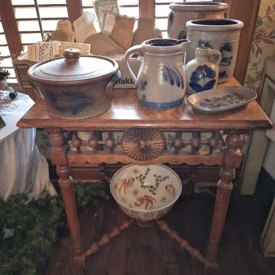 Sale Photo Thumbnail #39: Antique wooden side table featuring spindle legs and rosette detail, displayed with cobalt-decorated salt-glazed stoneware crocks, pitchers, and a patterned ceramic bowl below.