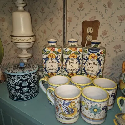 Sale Photo Thumbnail #16: Collection of hand-painted Italian Deruta-style ceramics, including three labeled liqueur decanters, matching mugs, and a blue decorative canister.