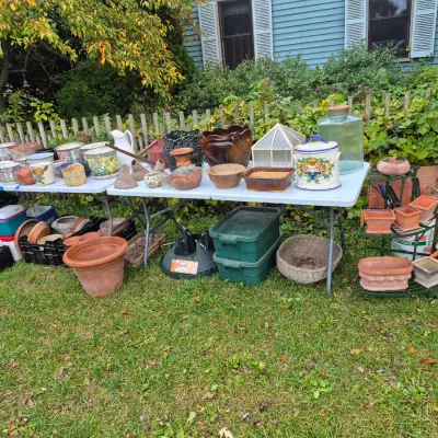 Sale Photo Thumbnail #313: Large assortment of outdoor and garden items including terra cotta pots, ceramic planters, glass terrariums, storage totes, and baskets displayed on folding tables.