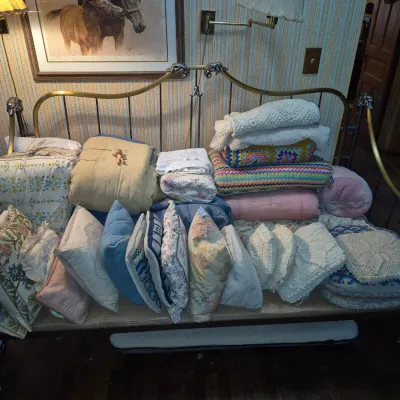 Sale Photo Thumbnail #91: Brass daybed filled with an assortment of vintage linens, throw pillows, quilts, and crocheted blankets.