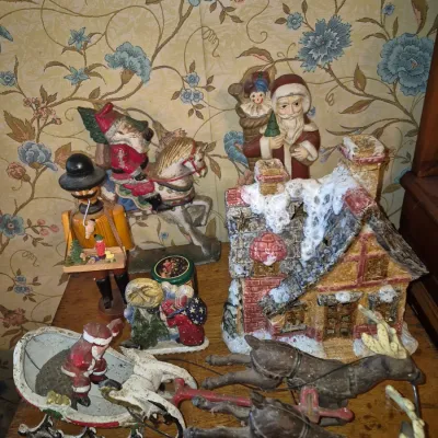 Sale Photo Thumbnail #2: Collection of vintage Christmas decorations, including a snow-covered cottage, Santa riding a horse, cast iron sleigh with reindeer, and traditional nutcracker figurines.
