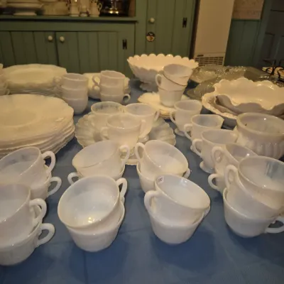 Sale Photo Thumbnail #18: Large collection of vintage white milk glass teacups, saucers, and serving bowls displayed on a blue tablecloth.