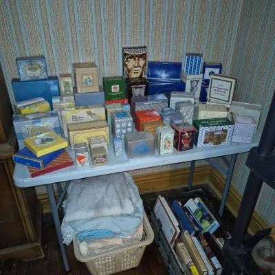 Sale Photo Thumbnail #98: Folding table display filled with vintage Avon cosmetic and gift boxes, with linens and a crate of books stored underneath.