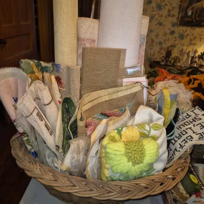 Sale Photo Thumbnail #4: Large wicker basket filled with various needlepoint canvas rolls, burlap, yarn, and unfinished crafting projects.