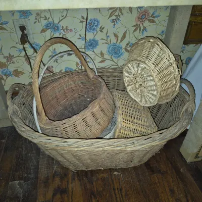 Sale Photo Thumbnail #49: Collection of vintage woven wicker baskets in various sizes and shapes resting under a table.