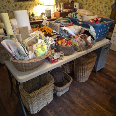 Sale Photo Thumbnail #77: Large assortment of crafting supplies, yarn, needlepoint canvases, and woven wicker storage baskets displayed on folding tables.