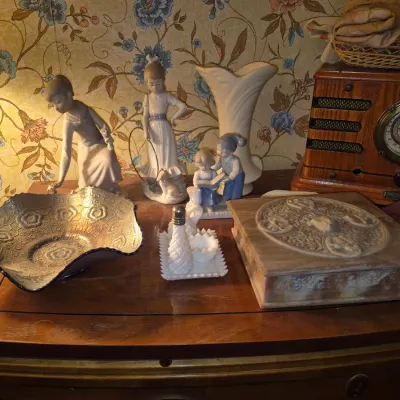 Sale Photo Thumbnail #69: Collection of decorative collectibles displaying porcelain figurines, a vintage-style Crosley radio, a carved stone box, milk glass salt and pepper set, and a iridescent glass bowl.