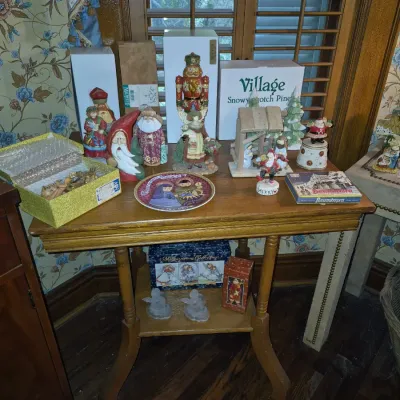 Sale Photo Thumbnail #50: Collection of holiday decorations, including a wooden nutcracker, nativity scene, Santa figurines, and decorative plates, displayed on a two-tier wooden side table.