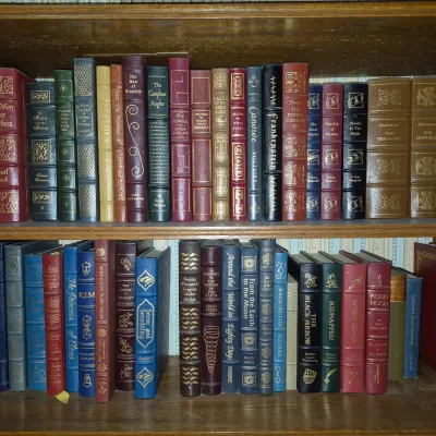 Sale Photo Thumbnail #6: Two wooden bookcase shelves filled with a collection of decorative leather-bound classic literature hardcovers.