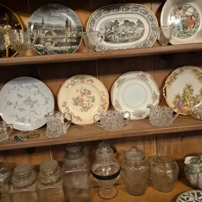 Sale Photo Thumbnail #268: Collection of vintage decorative plates, pressed glass creamers and sugar bowls, and assorted glass storage jars displayed on wooden shelves.