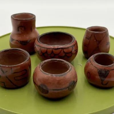 Sale Photo Thumbnail #9: Collection of six miniature terracotta pottery vessels with hand-painted black geometric designs, displayed on a green tray.