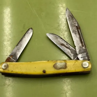 Sale Photo Thumbnail #17: Vintage multi-blade pocket knife with a yellow synthetic handle, showing significant wear, rust, and patina on the blades.