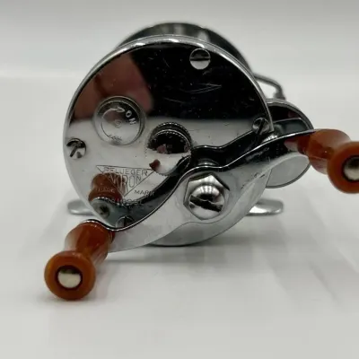 Sale Photo Thumbnail #26: Vintage Pflueger Akron No. 1893L baitcasting fishing reel with a chrome finish and amber-colored handles.