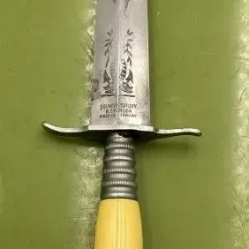 Sale Photo Thumbnail #20: Vintage Solingen Cutlery dagger featuring an etched steel blade, a simple crossguard, and a ribbed metal handle with yellow celluloid accents.