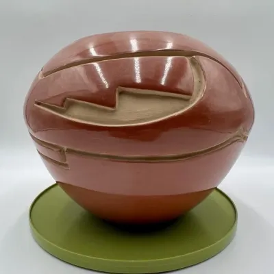 Sale Photo Thumbnail #6: Southwestern-style carved redware pottery vessel, featuring geometric step designs and a polished finish, displayed on a green stand.