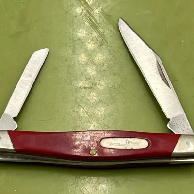 Sale Photo Thumbnail #18: Vintage Buck 305 Lancer pocket knife featuring a red handle with silver-tone bolsters and two folding blades, showing some wear from use.