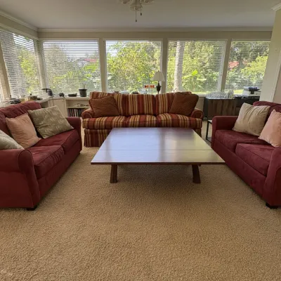 Living room seating set including a large square wooden coffee table, two burgundy fabric sofas, and a red and gold striped upholstery sofa.