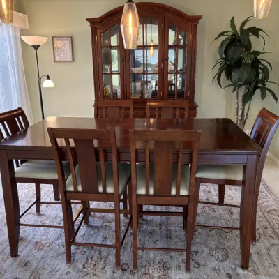Traditional dark wood dining set including a high-top table, six matching upholstered chairs, and a large display hutch cabinet.