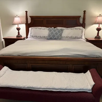 Traditional wooden four-poster king bed frame set, flanked by matching two-drawer nightstands with urn-style table lamps.