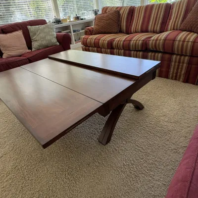 Contemporary dark wood expandable coffee table with curved legs, featured in a sunroom with plush seating.