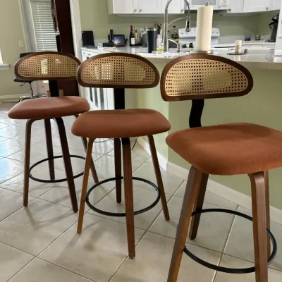 Set of three mid-century modern style swivel counter stools featuring woven cane backrests, terracotta fabric seats, and dark wood legs...
