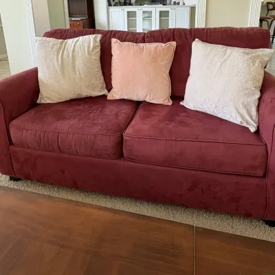 Burgundy microfiber two-cushion loveseat with three accent pillows, including two beige and one pink.