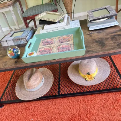 Rustic industrial coffee table with black metal frame, displaying assorted picture frames, a green wooden tray, and straw sun hats on the...