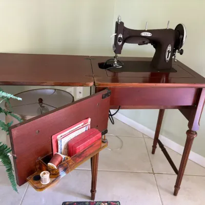 Vintage White electric sewing machine built into a wooden fold-out cabinet, complete with attached storage rack holding sewing accessories.