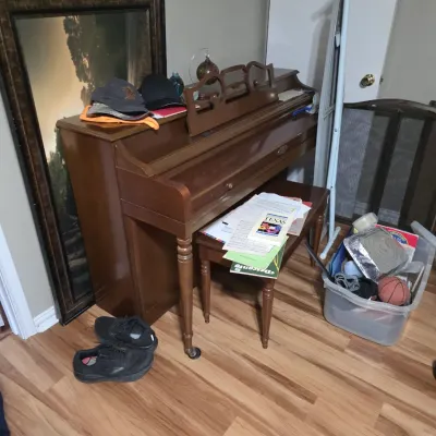 Sale Photo Thumbnail #5: Vintage Baldwin spinet piano with matching wooden bench, shown alongside various household items including a framed mirror, hats, and sheet music.
