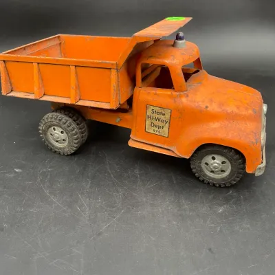 Vintage orange pressed steel toy dump truck labeled "State Hi-Way Dept 975," showing moderate wear and paint loss consistent...
