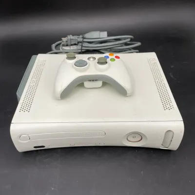 Original model white Microsoft Xbox 360 console with a matching wireless controller and power cable, showing some light wear and...