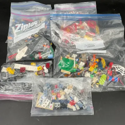 Assorted Lego bricks, minifigures, and specialty pieces sorted into five clear plastic storage bags.