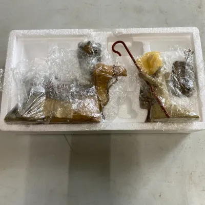 Nativity scene figurines, including a camel and a shepherd with a staff, wrapped in protective plastic and stored in a styrofoam insert.