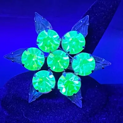 Vintage uranium glass flower brooch glowing bright green under a UV blacklight.