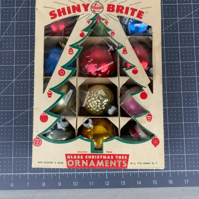 Vintage box of Shiny Brite glass Christmas tree ornaments, featuring an assortment of colorful, patterned, and textured baubles in their...