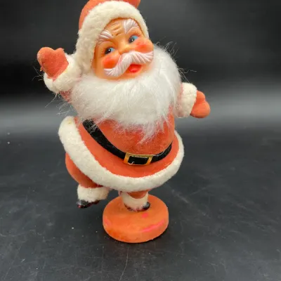 Vintage mid-century Santa Claus figurine with a flocked suit, plastic face, and faux fur beard, standing on a round orange base in a...