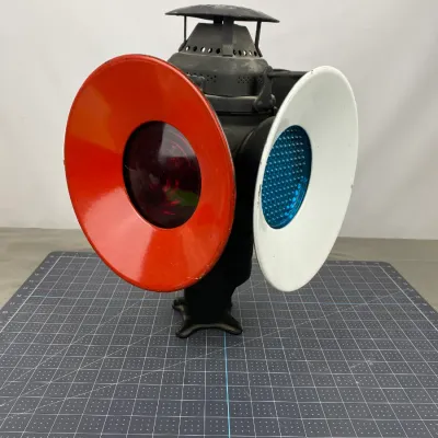 Vintage railroad switch lantern featuring a black metal body, a red-rimmed lens, and a white-rimmed blue lens.