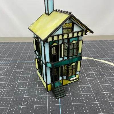 Vintage stained glass house lamp featuring a Victorian-style design with blue, yellow, and green glass panels.