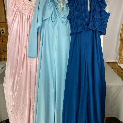 Three vintage 1970s nightgowns and robes in pink, light blue, and royal blue, featuring lace details and pleated accents.