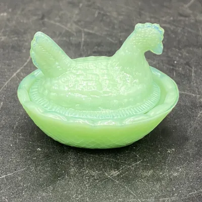 Vintage miniature green slag glass hen on nest covered dish, showing a textured basketweave base and detailed feathering on the lid.