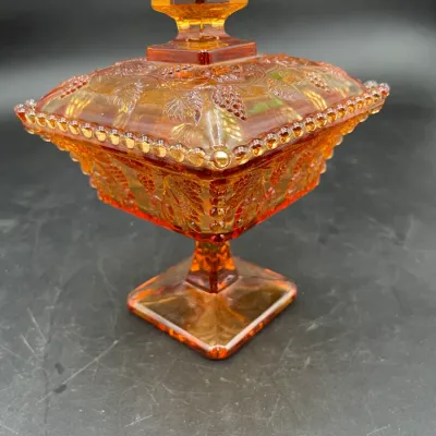 Vintage marigold carnival glass footed candy dish with lid, featuring an embossed grape and leaf pattern with beaded edges.