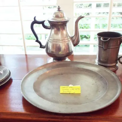 Collection of antique pewter hollowware and tableware, including a lidded coffee pot, pitchers, mugs, plates, and a large round serving...