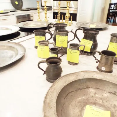 Collection of vintage and antique pewter serveware, including various sized tankards, mugs, plates, and bowls, displayed alongside brass...