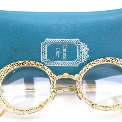 Vintage Christian Dior round eyeglasses featuring intricate gold-tone filigree frames, accompanied by a teal blue branded soft case.