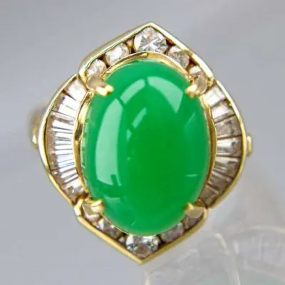 Vintage gold ring featuring a large oval cabochon green jadeite jade stone, accented by a halo of baguette and round-cut diamonds.