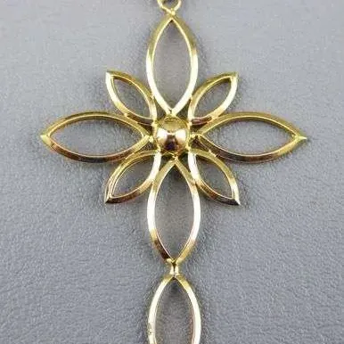 Gold-tone openwork cross pendant featuring a stylized floral center and marquise-shaped loops, shown on a textured grey background.