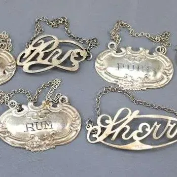 Collection of eight vintage silver-plated decanter labels with hanging chains, featuring embossed and cutout lettering for various...
