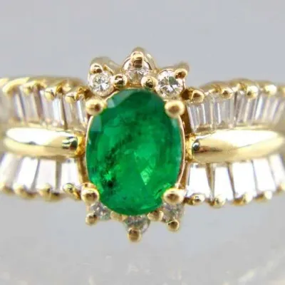 Vintage 14k yellow gold ring featuring a central oval-cut emerald accented by small round diamonds and flanked by tapered baguette...