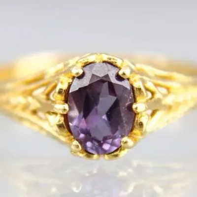 Vintage gold ring featuring an oval-cut purple gemstone, possibly amethyst, set in an ornate filigree band.